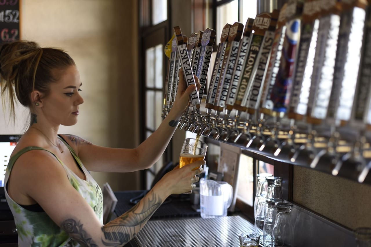 Bartender pouring from a tap handle at a taproom bar.