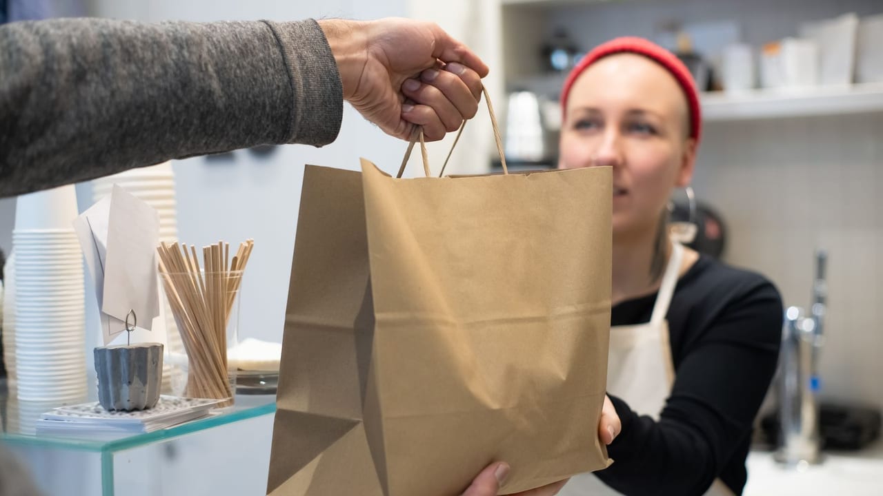 Restaurant worker handing a labelled takeaway bag to a customer.