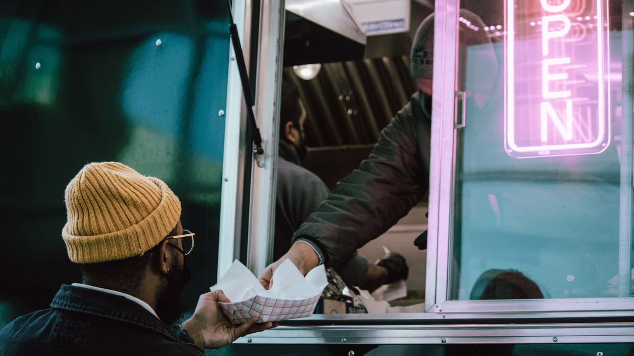 Customer collecting a bagged order at a food truck window.