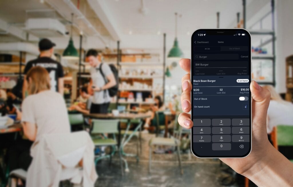 Manager holding their phone in a busy restaurant editing the on hand count of a menu item