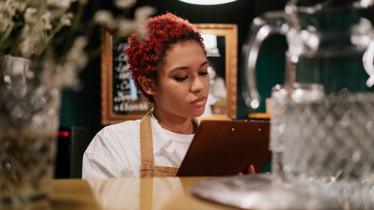 Restaurant staff member checking a clipboard against the menu board.